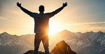 A person standing on a mountain at sunrise with arms raised.
